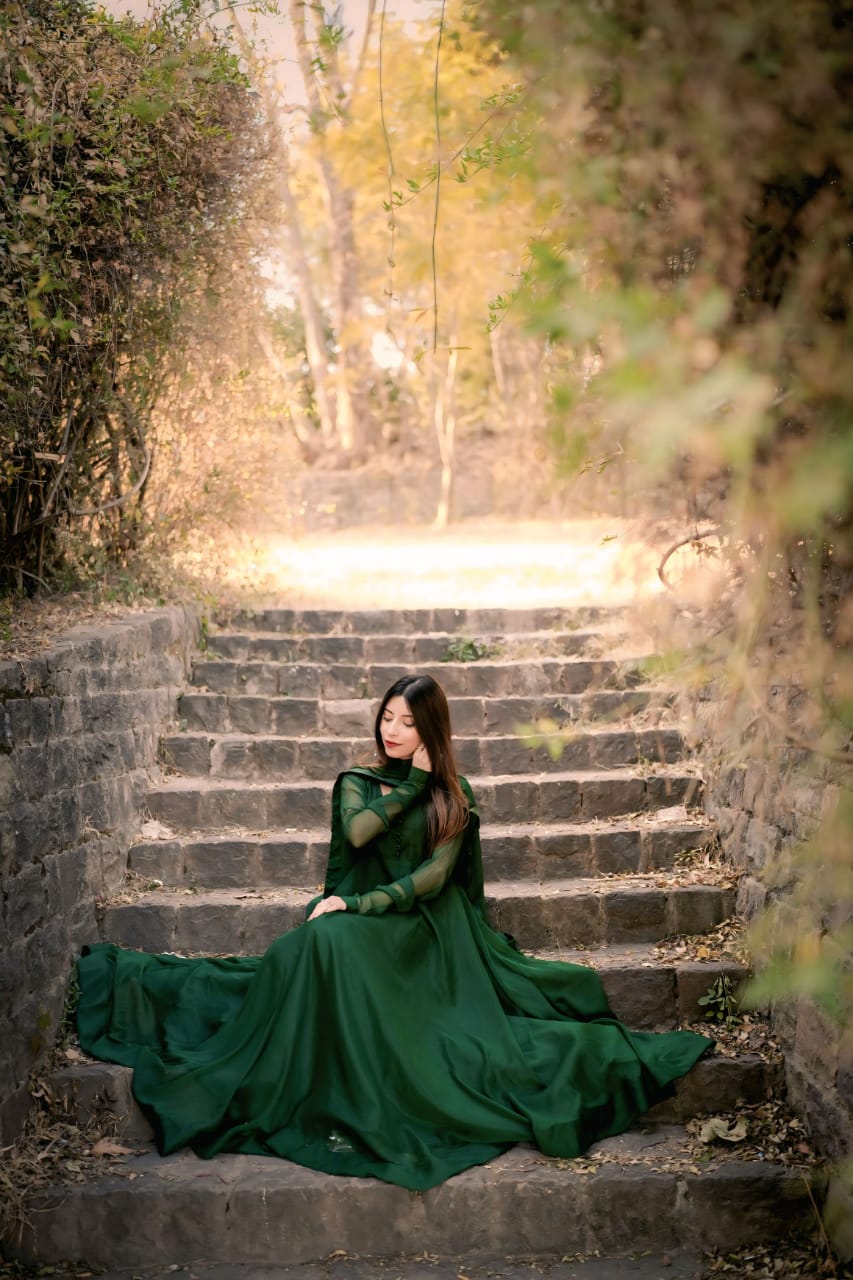 Seated staircase view of Abroo green chiffon frock showing the wide flare, flowing hem and matching chiffon dupatta