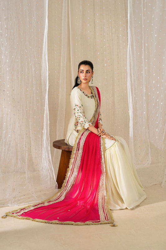 Seated model wearing the Dove Blossom ivory embroidered gharara set with a shocking pink chiffon dupatta