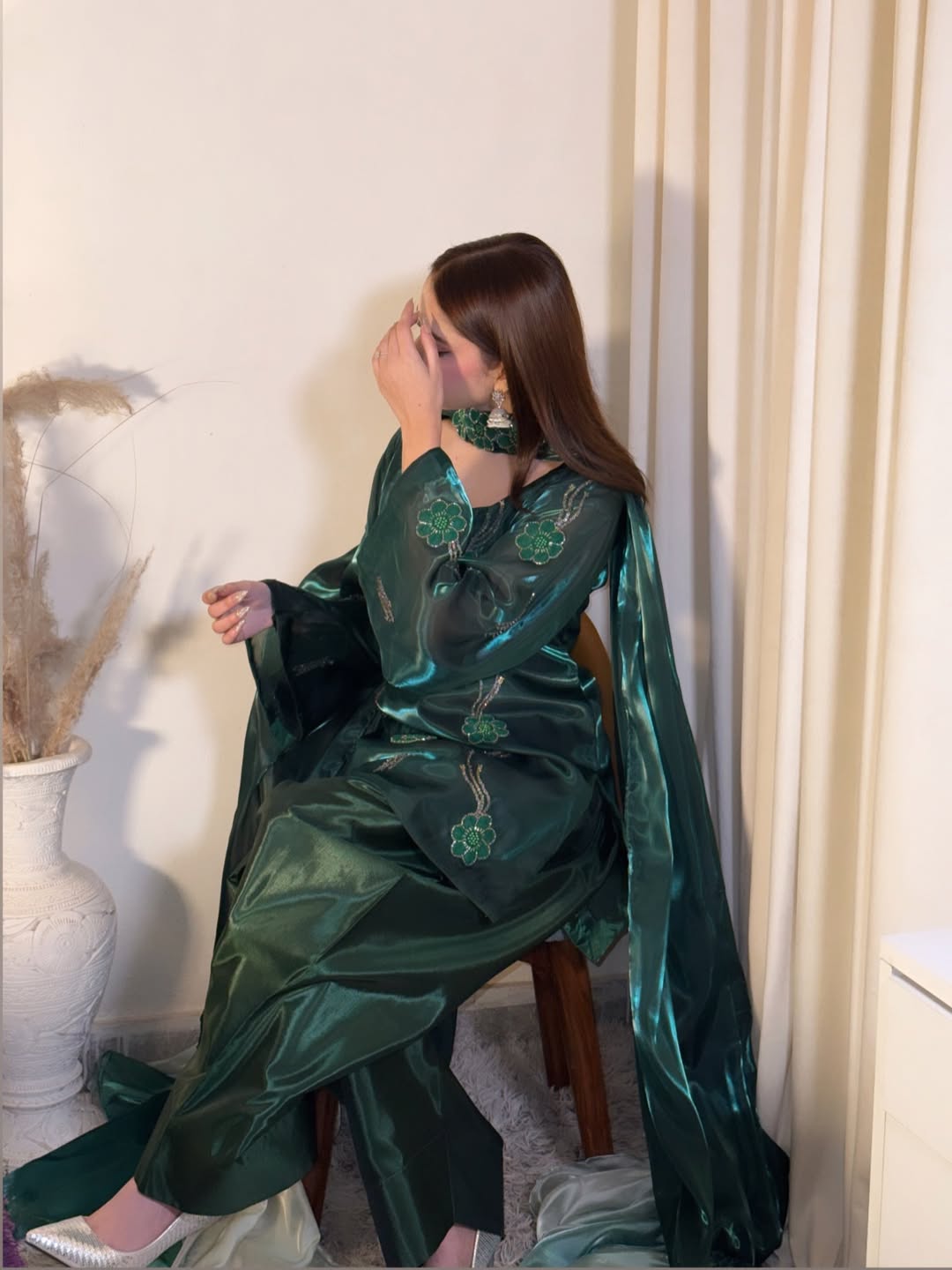 Seated model displaying the flowing drape and wide cape sleeves of an emerald green Anabiyawear outfit
