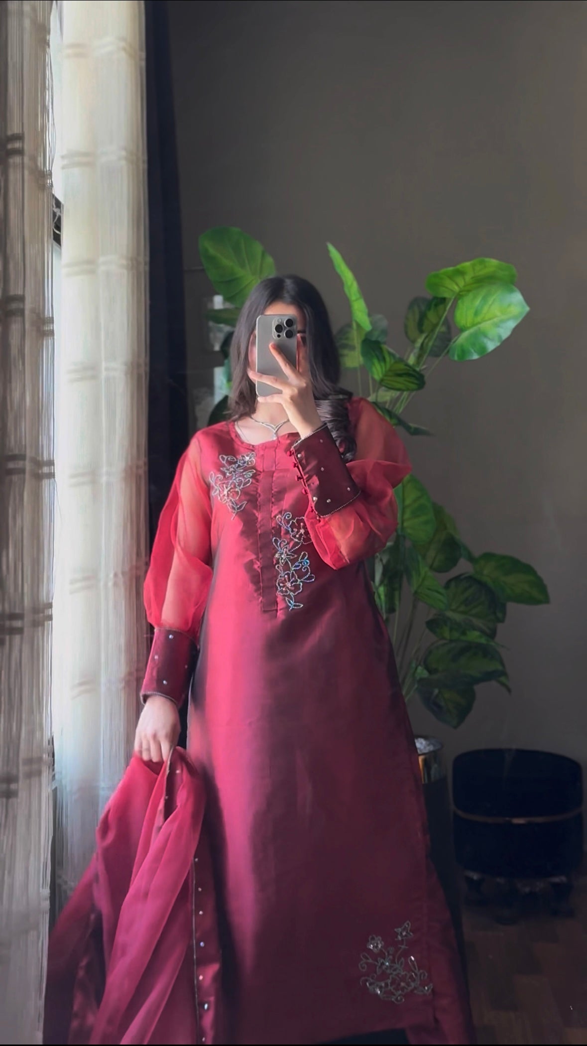 Murraya Maroon China katan silk three piece suit in a mirror pose with crystal chain motifs, long shirt and organza dupatta