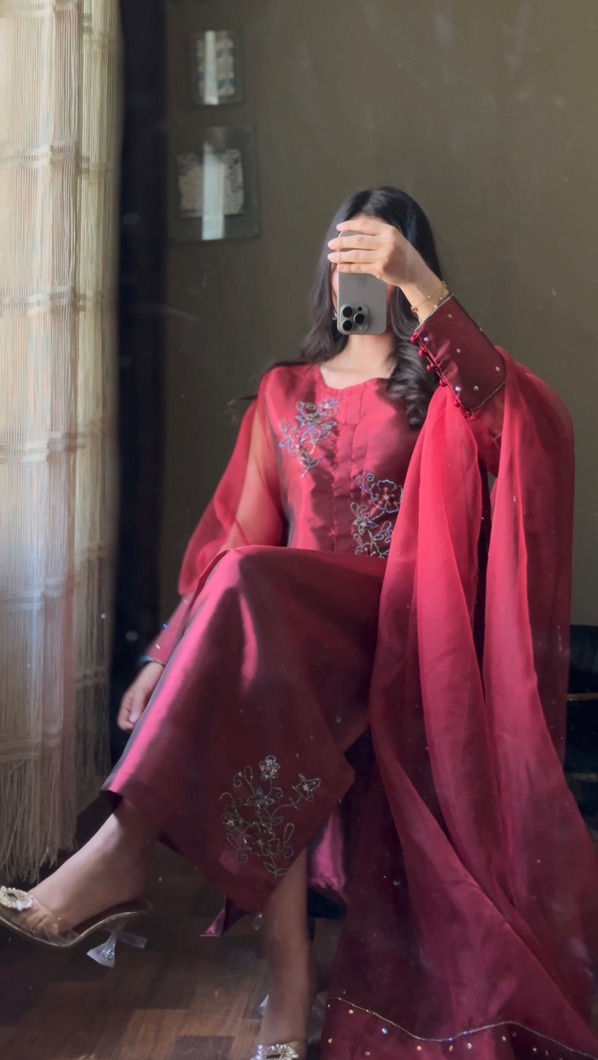 Seated view of Murraya Maroon katan silk three piece suit with organza dupatta, crystal chain motifs and embellished maroon shirt
