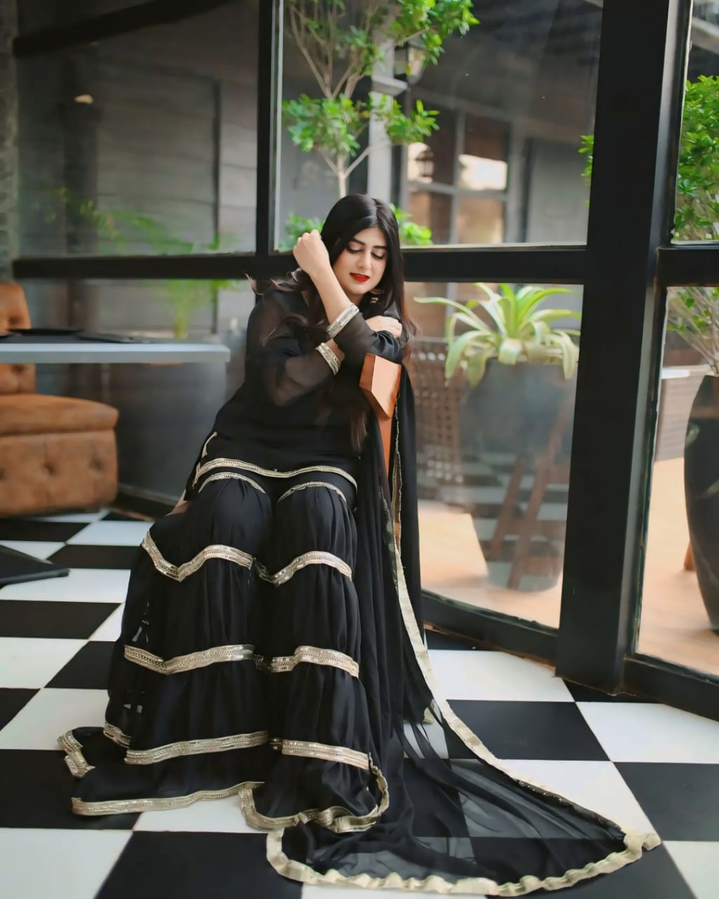 Rebel black chiffon garara suit in seated side pose with layered golden lace and flowing dupatta by Anabiyawear
